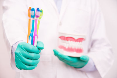 Midsection of dentist holding dentures and toothbrushes