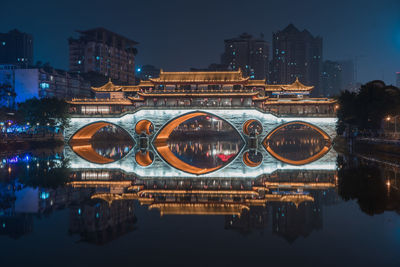 Illuminated arch bridge over river in city at night