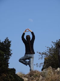 Woman making heart shape while standing against clear sky