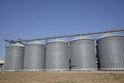 Low angle view of silos against clear blue sky during sunny day