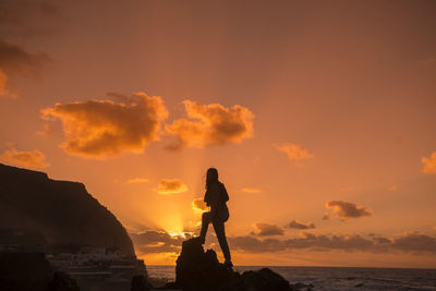 Silhouette people standing on rock by sea against sky during sunset