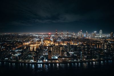 Aerial view of illuminated cityscape by river against sky at night