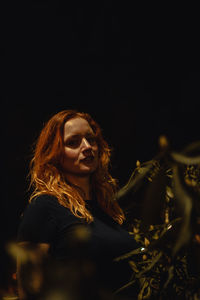 Portrait of young woman looking away against black background