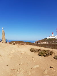 Lighthouse by sea against clear blue sky