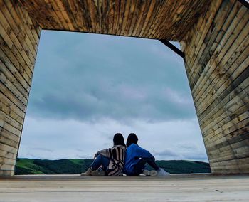 Rear view of men sitting on bridge against sky