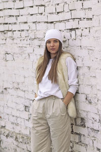 A girl in white clothes stands against a white brick wall.