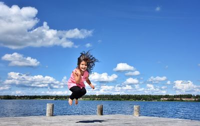 Full length of happy woman jumping in lake against sky