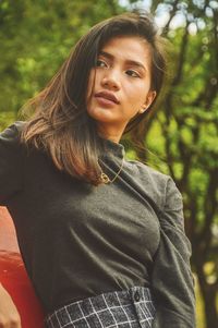 Young woman looking away while sitting against trees