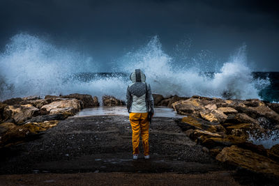 Rear view of man standing on rock by sea