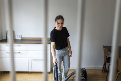 Smiling young woman using vacuum cleaner at home