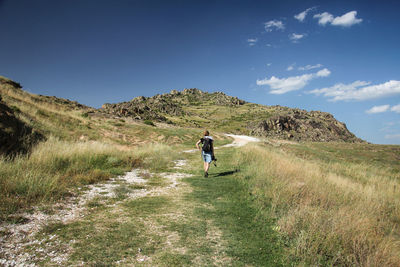 Full length rear view of woman walking on field against sky