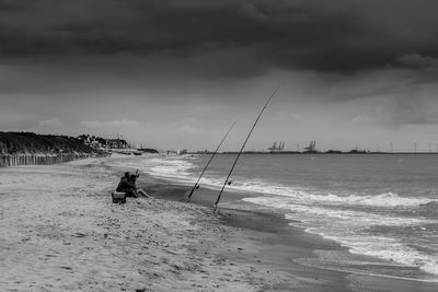 Man fishing on beach against sky