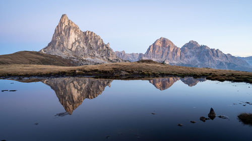 Rocky mountains reflected in small still pond serving as a mirror during sunrise , dolomites, italy