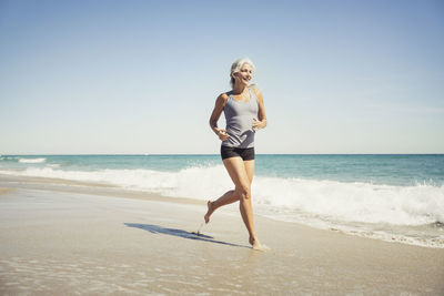 Full length of mature woman jogging on sea shore at delray beach