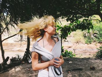 Woman with tousled hair standing against trees