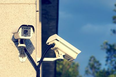 Low angle view of security cameras on wall against sky