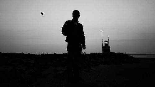 Silhouette man standing by sea against sky during sunset