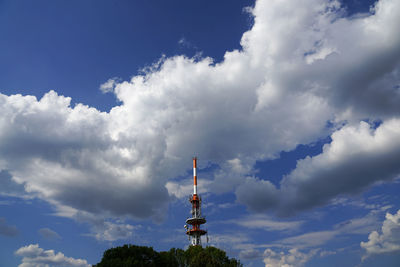 Low angle view of communications tower amidst buildings against sky