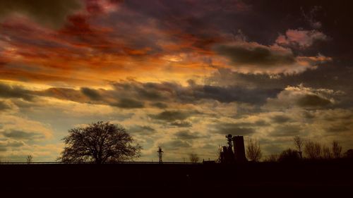 Silhouette trees and buildings against dramatic sky