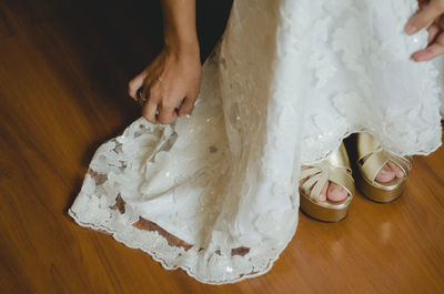 Low section of bride wearing sandals on hardwood floor