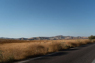 Dirt road along landscape against clear blue sky