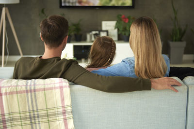 Rear view of family watching tv while sitting on sofa at home