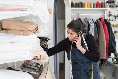 Mature female dry cleaner talking on smart phone while working at laundromat