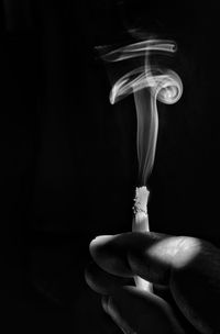 Close-up of hand holding cigarette against black background