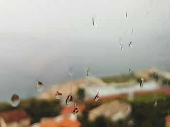 Close-up of wet glass window against sky during rainy season