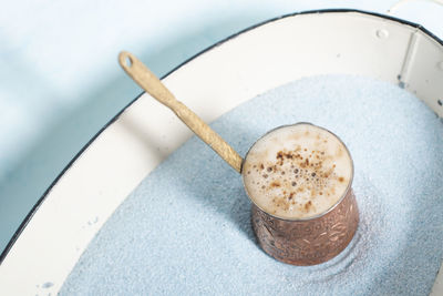 Copper coffee pot with hot coffee on blue sand, coffee break, turkish coffee