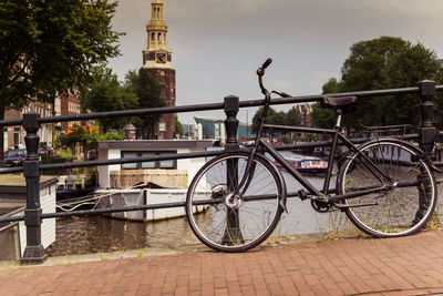 Bicycle by railing in canal against sky