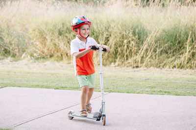 Portrait of boy standing in push scooter on footpath