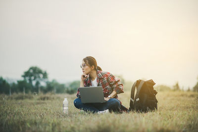 Rear view of woman using laptop while sitting on field