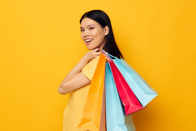 Portrait of young woman holding shopping bags against yellow background