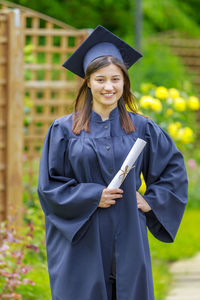 Portrait of young woman in graduation gown standing at park