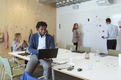 Businessman using laptop while sitting with colleagues at board room