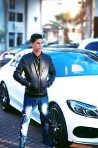 Young man standing by car in city