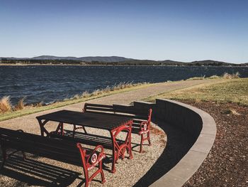 Empty bench by sea against clear sky