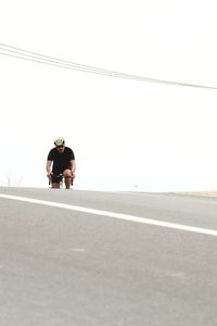 Man riding bicycle on road against clear sky