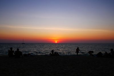 Silhouette people on beach against sky during sunset