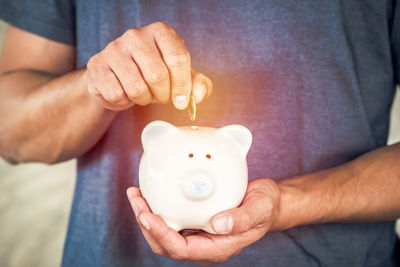 Midsection of man holding glowing coin on piggy bank