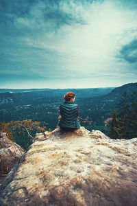 Rear view of woman sitting on landscape against sky