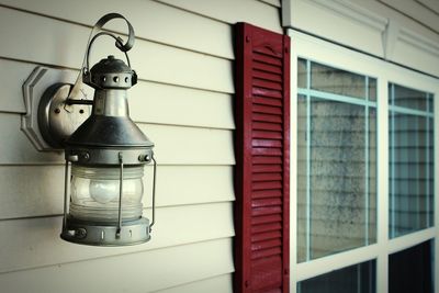 Close-up of electric lamp hanging on wall with a shutter and window.