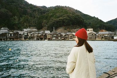 Rear view of woman standing by sea against mountain