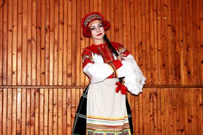 Portrait of woman in traditional dress posing against wooden wall