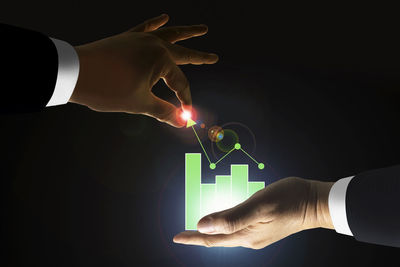 Close-up of hand holding illuminated lighting equipment against black background