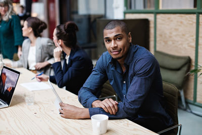 Portrait of young businessman sitting with female colleagues at table in office meeting