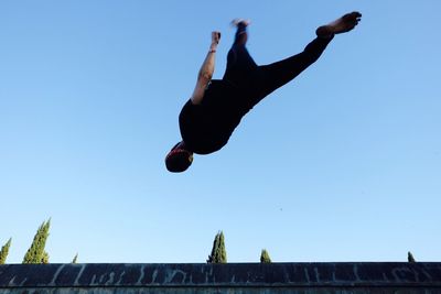 Low angle view of man jumping against clear sky