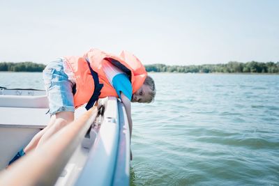 Young boy dipping his hand in the water whilst on a boat in summer