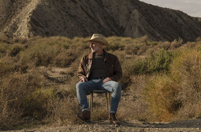Adult man in cowboy hat sitting on abandoned chair in desert, almeria, spain
